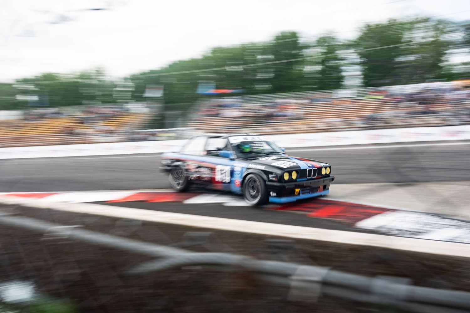 Classic BMW racing car in blue and white livery competes on a racetrack during a motorsport event.