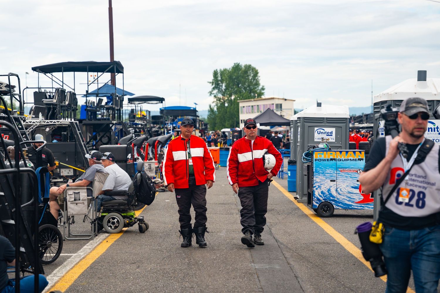Emergency responders and police officers gather around vehicles and equipment at an outdoor event scene during daytime.