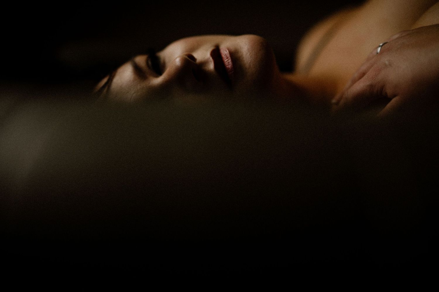 Person lying down in dramatic shadow and low lighting creating a moody atmospheric portrait.