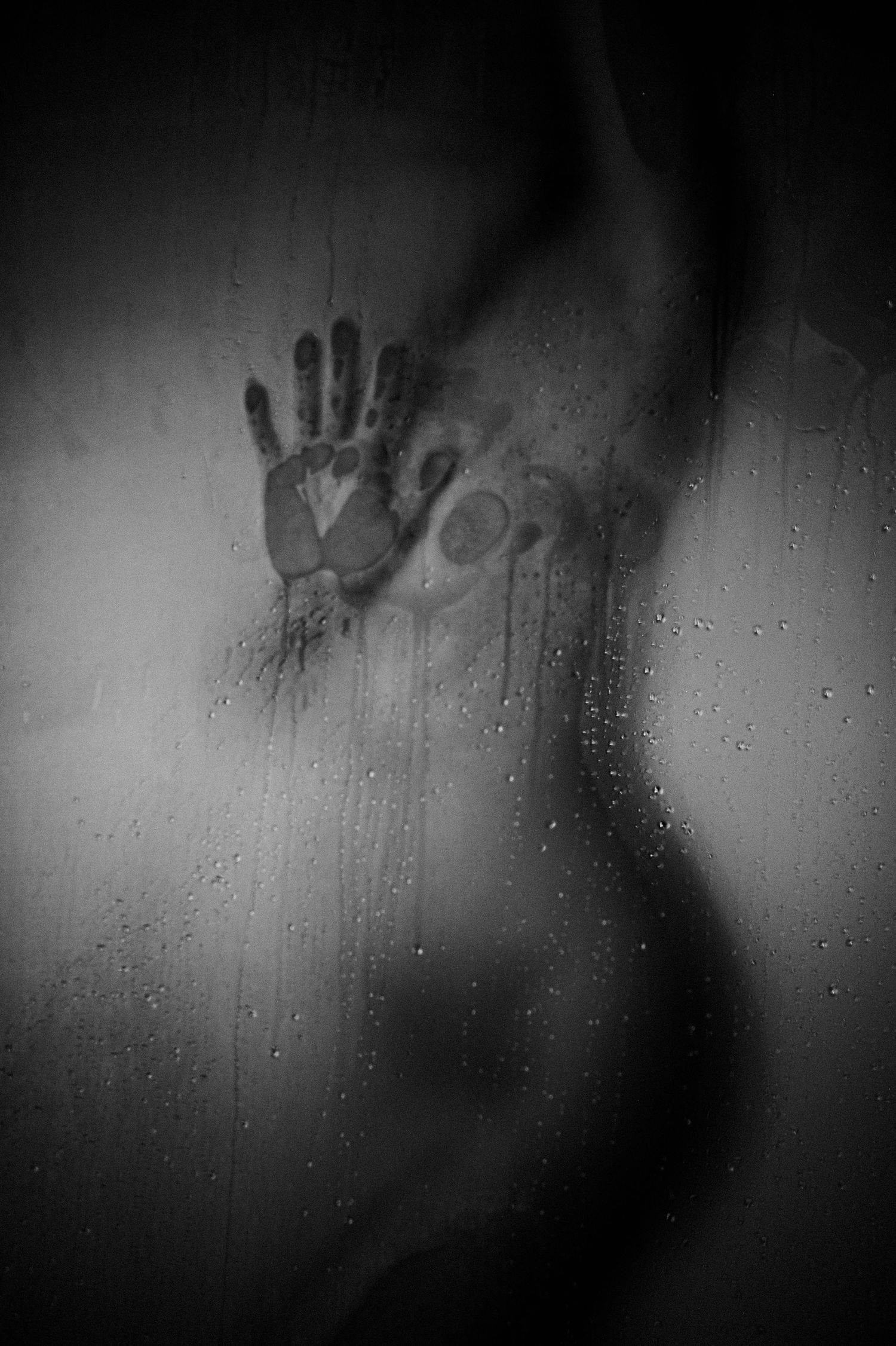 Creepy silhouette and handprint on frosted glass with water droplets in black and white.