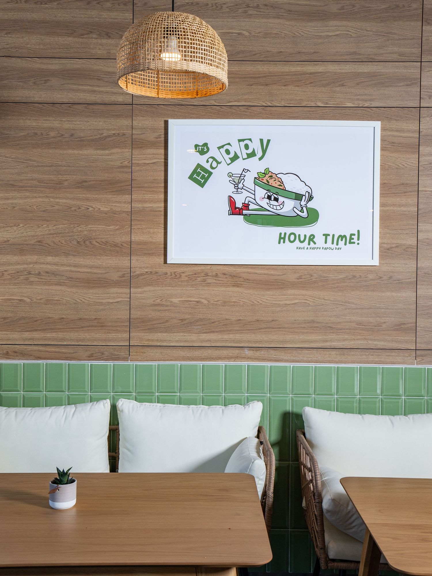 Modern restaurant interior with wooden walls, green tile backsplash, and cartoon illustration on wall under a rattan pendant light.