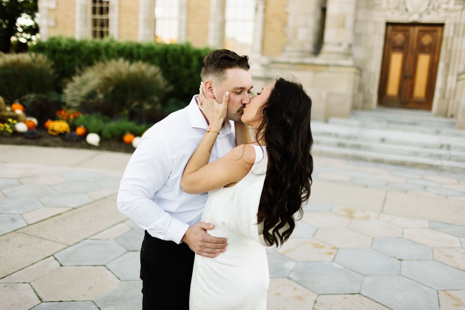 A newly married couple shares a romantic kiss on the steps of an elegant stone building with blooming flowers nearby taken in Guelph Ontario