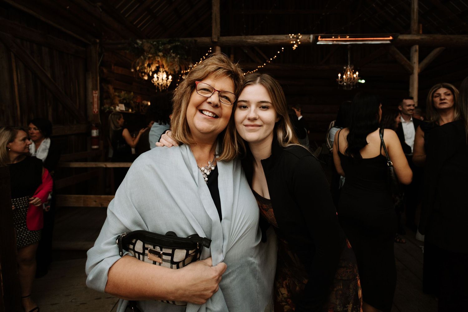 Two people smiling together at an evening indoor celebration with warm lighting and rustic decor in the background.