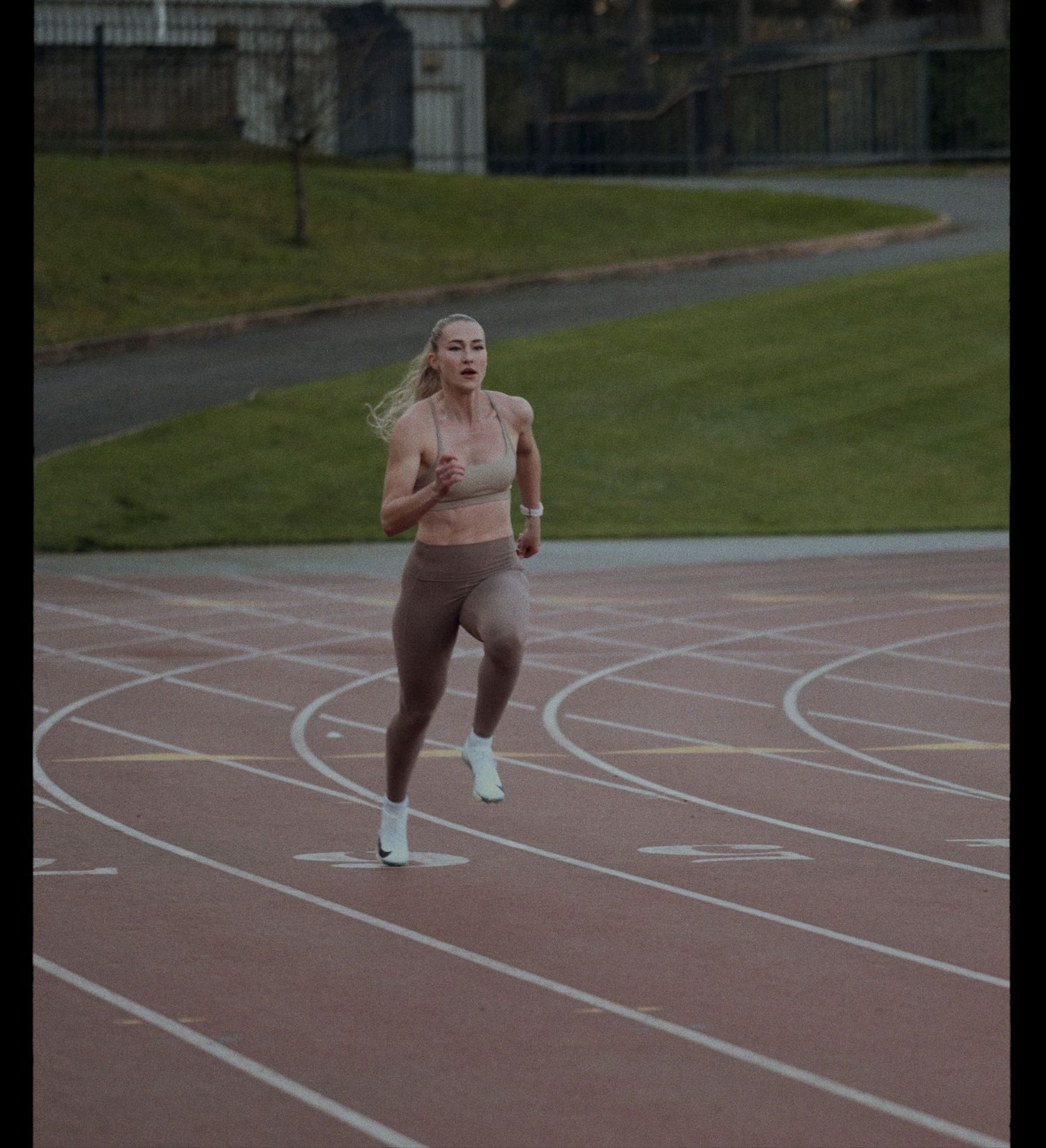 Athlete running on an outdoor track curve during training session at dusk.