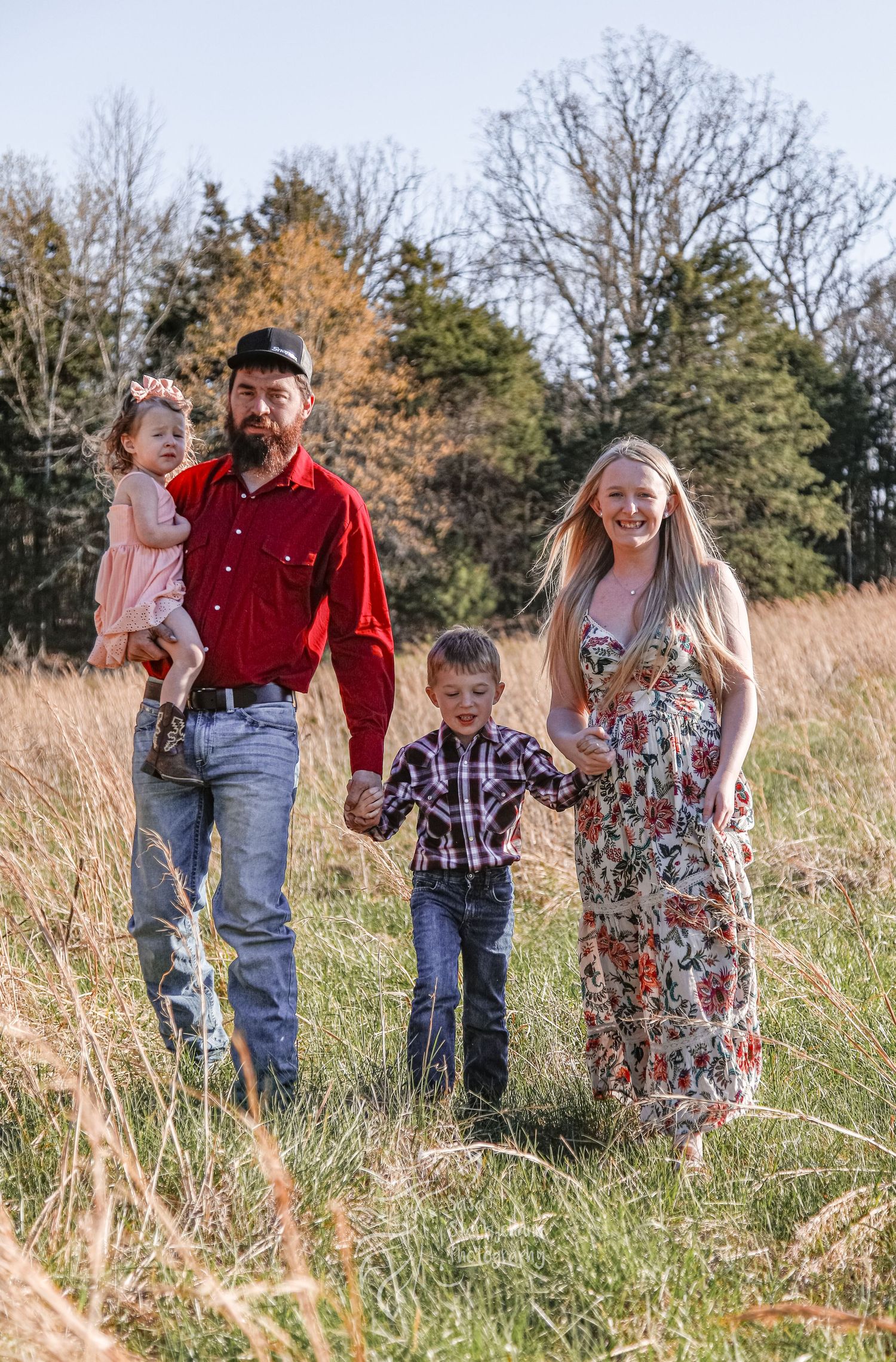 A family portrait taken in a rustic field with autumn trees in the background.