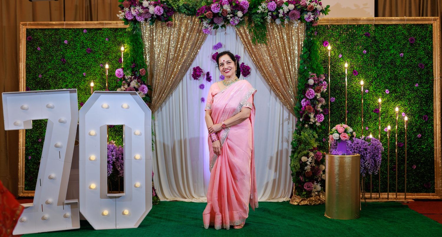 Wedding photo backdrop featuring illuminated number 70 with green wall and floral decorations.