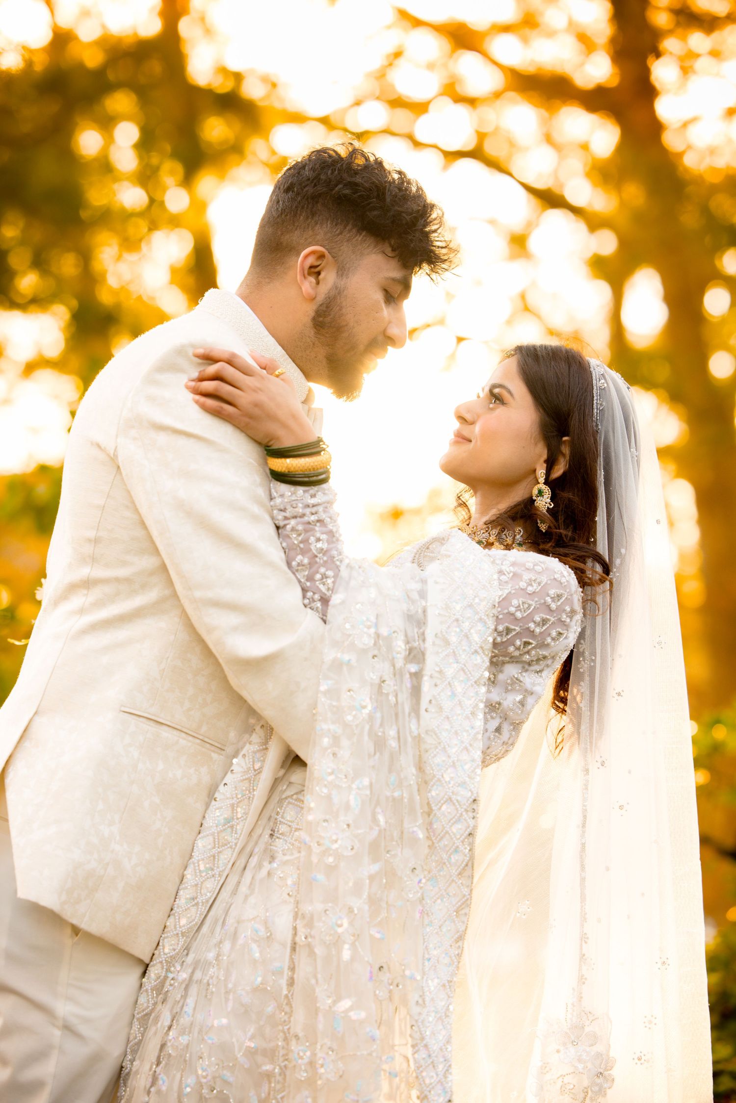 A romantic wedding couple embrace during golden hour with glowing autumn trees behind them.