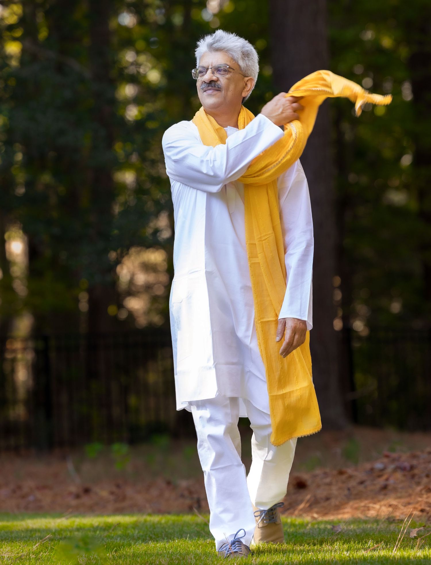 Person in white kurta holding yellow fabric outdoors in wooded setting.