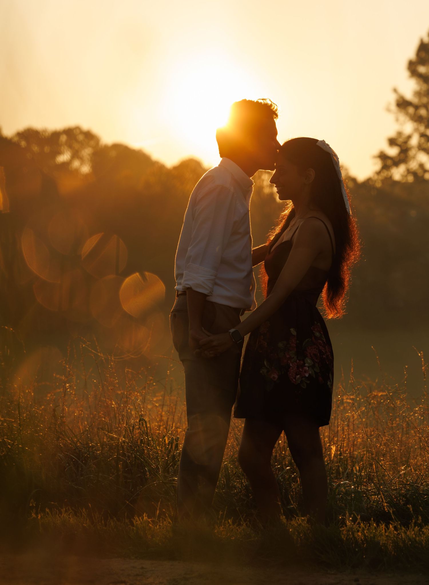 A silhouetted couple shares an intimate moment at sunset in a field of tall grass.