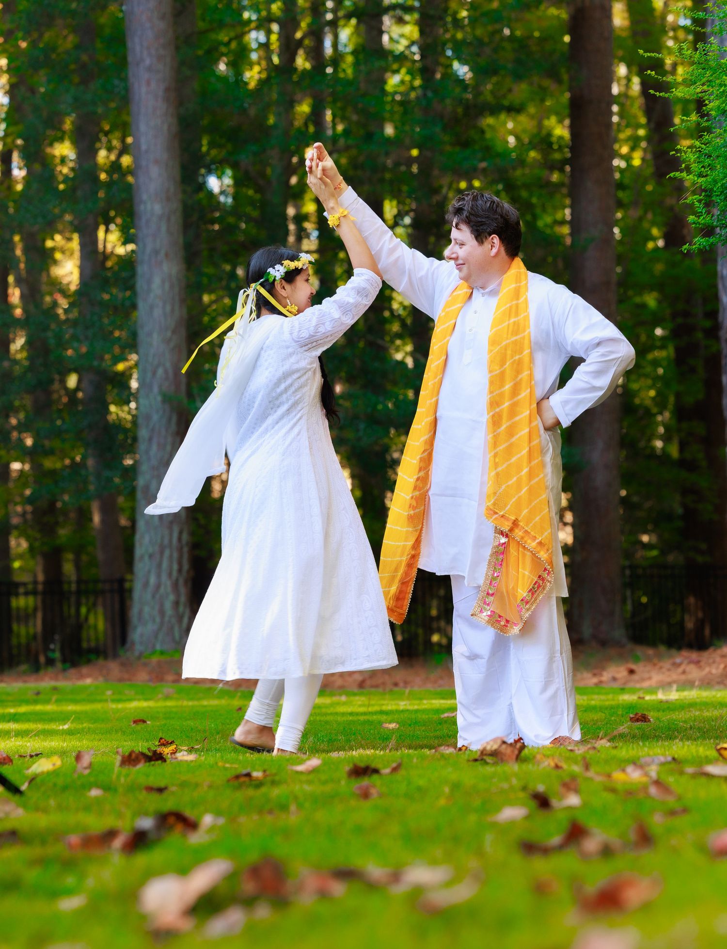 A dance celebration in traditional white outfits with yellow scarf against a forest backdrop.