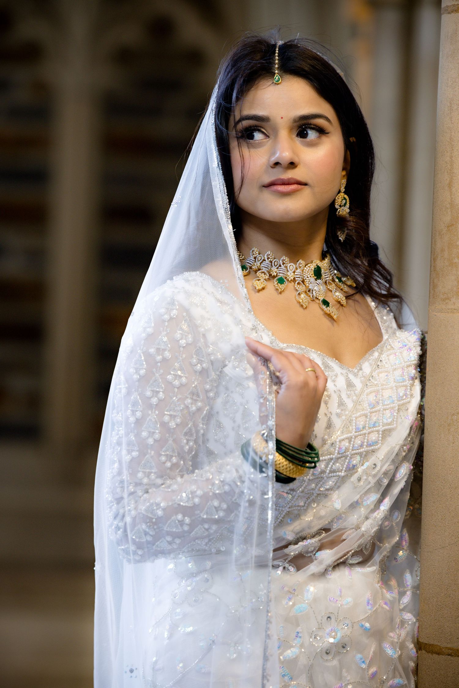 Bride in elegant white and silver saree with statement jewelry looking to the side.