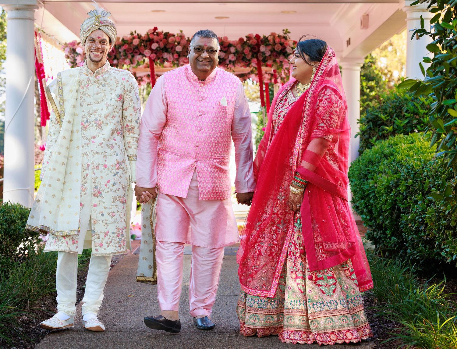 Traditional Indian wedding scene with guests in colorful formal attire under decorated pink canopy.