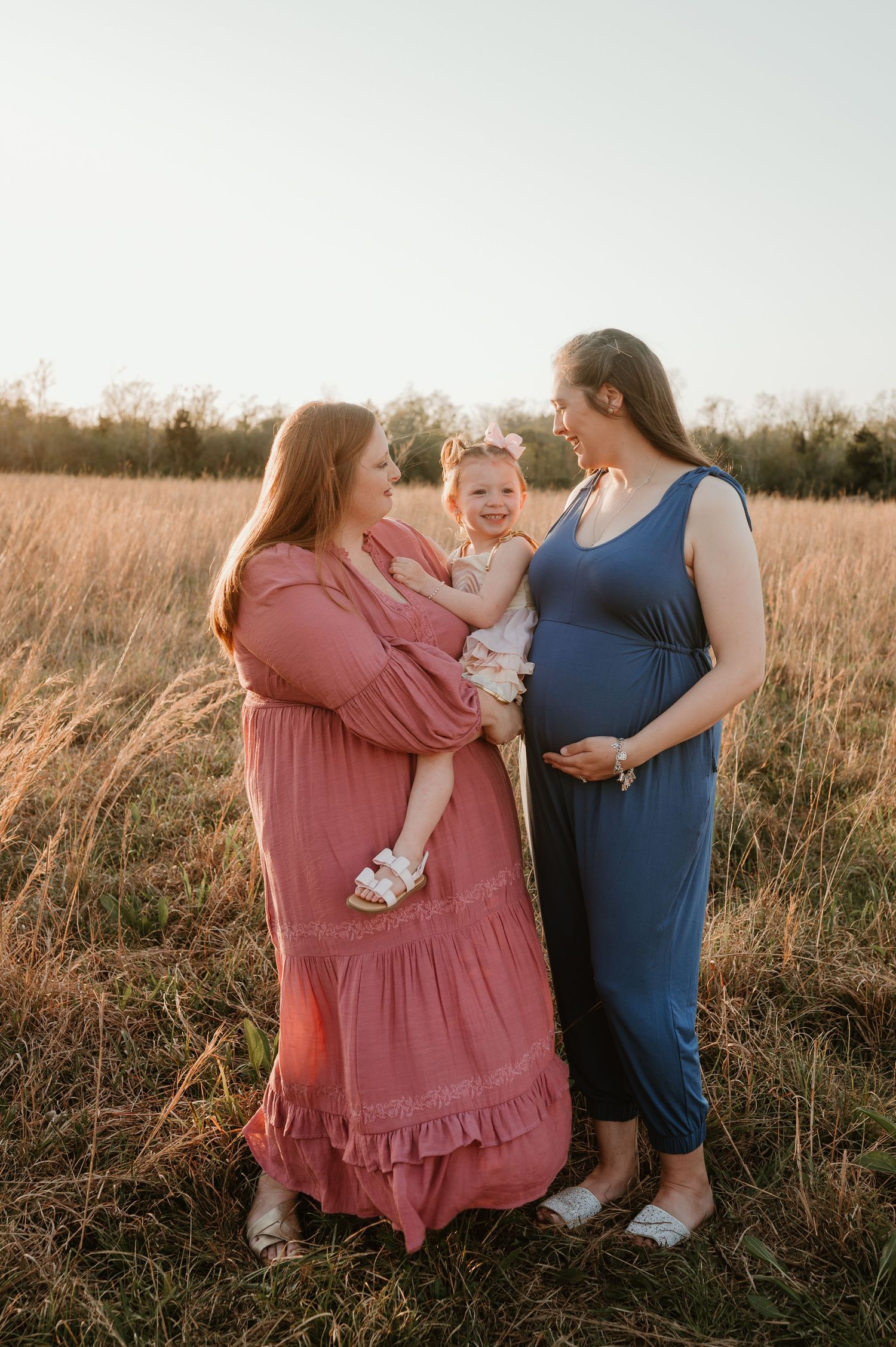 Two mothers laughing and smiling with their 3 year old daughter during a family session