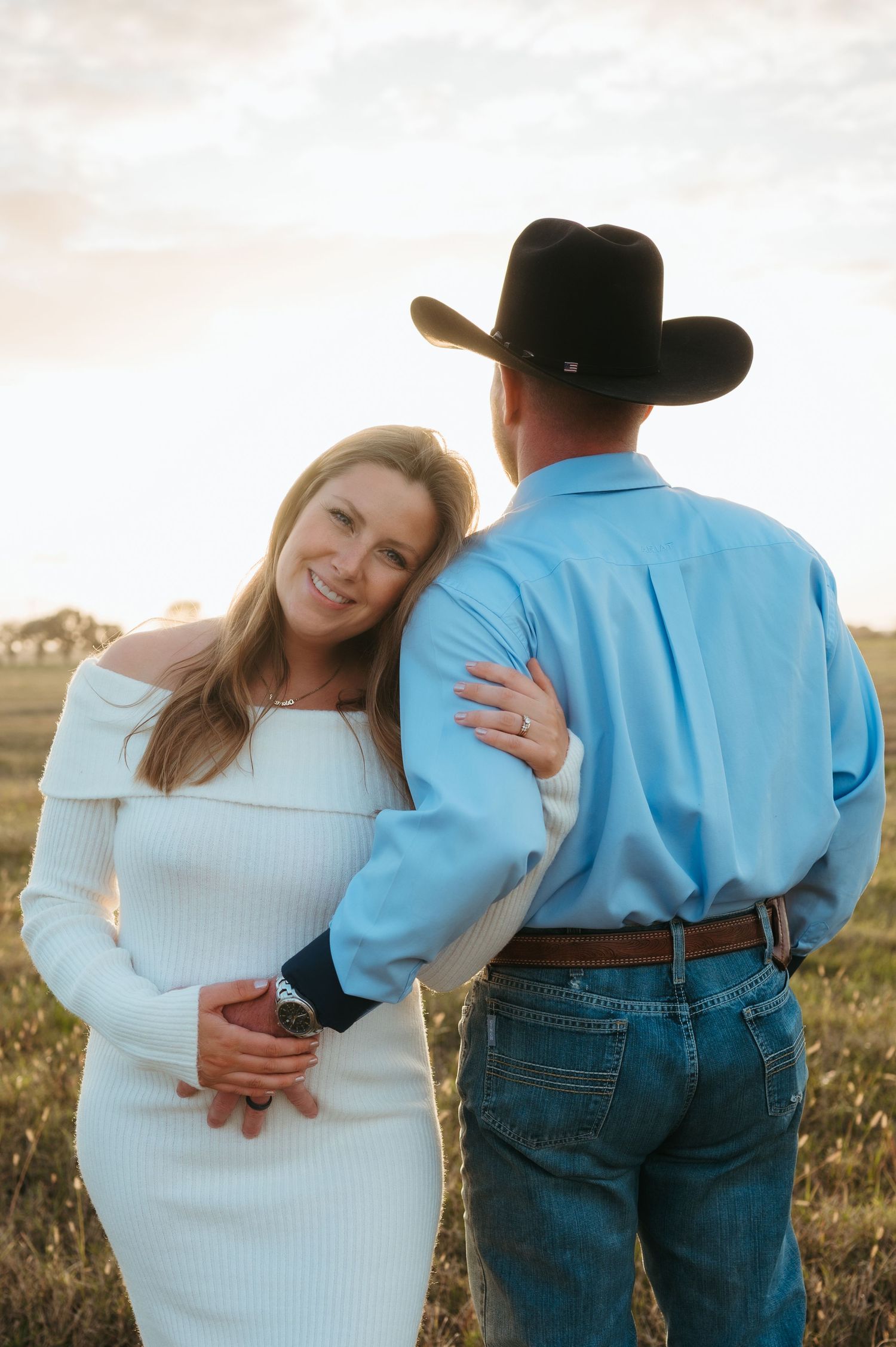 A beautiful mother to be embraces her husband while he places his hand on her growing belly during a maternity session