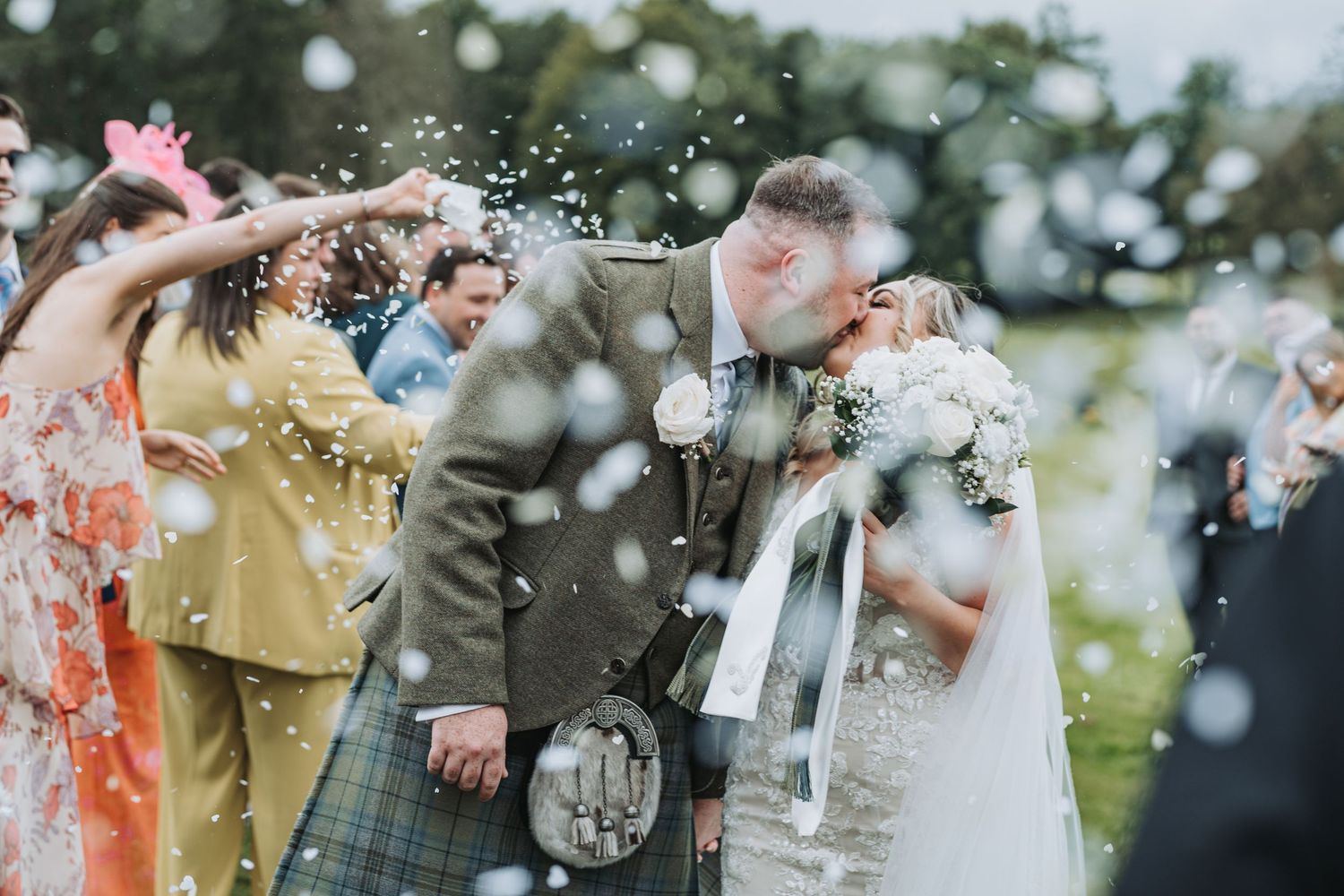 Wedding guests throw confetti over newlyweds in a joyful outdoor celebration with the groom wearing a traditional kilt at Cornhill Castle