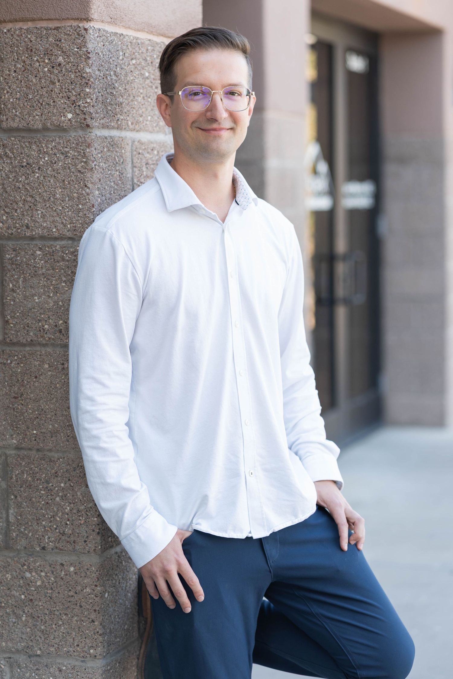 guy with glasses, wearing a white long sleeved shirt, standing against the wall