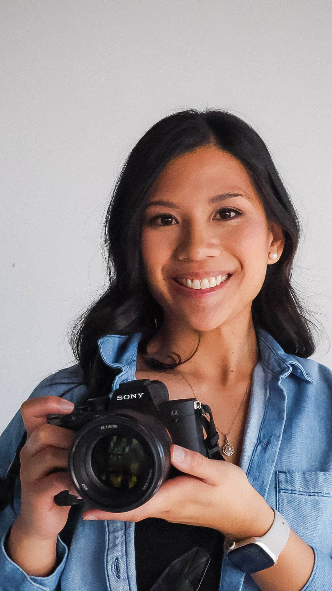 girl wearing a blue button up, smiling and holding Sony camera