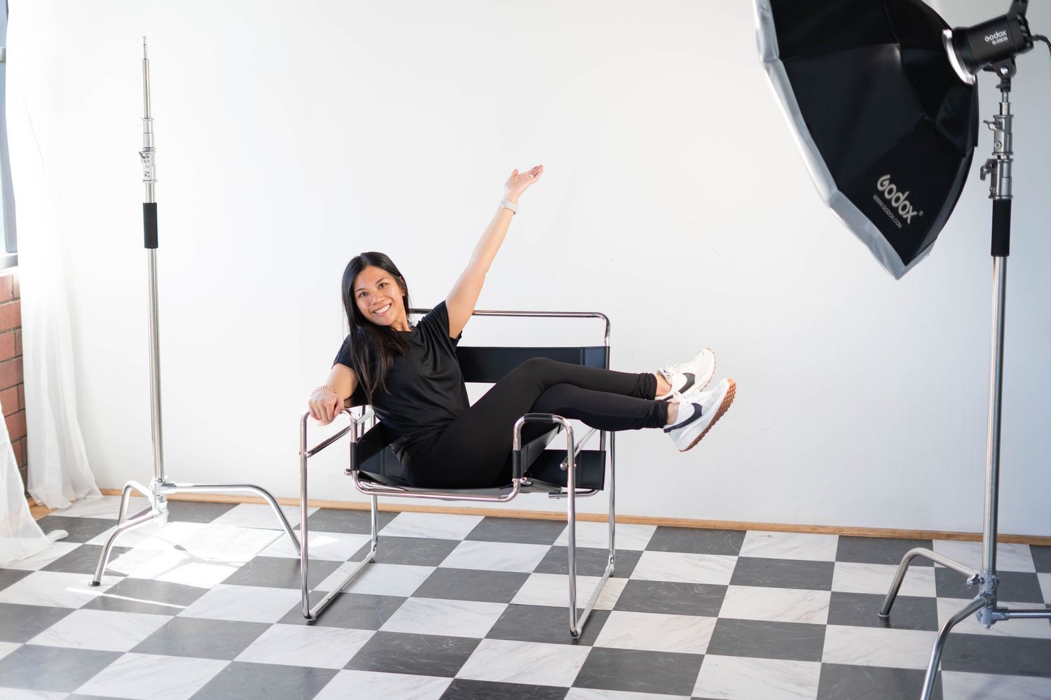 girl sitting on a black metal chair, legs crossed, wearing white and black nike shoes, godox strobe studio lights