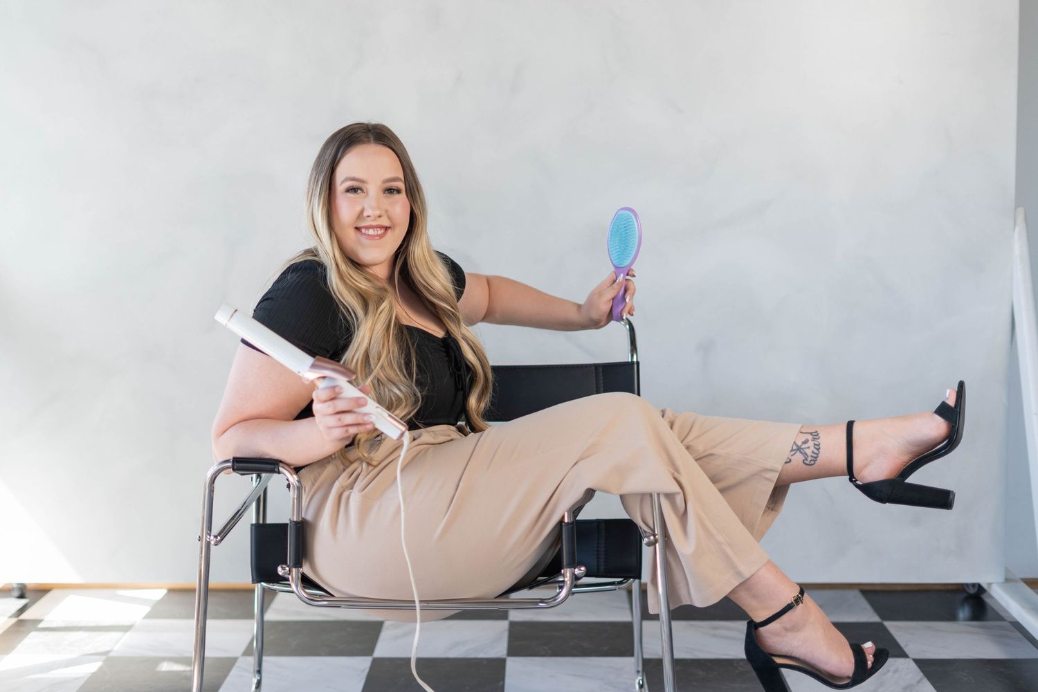 girl with a curling tool and a brush, girl sitting on a black, metal chair