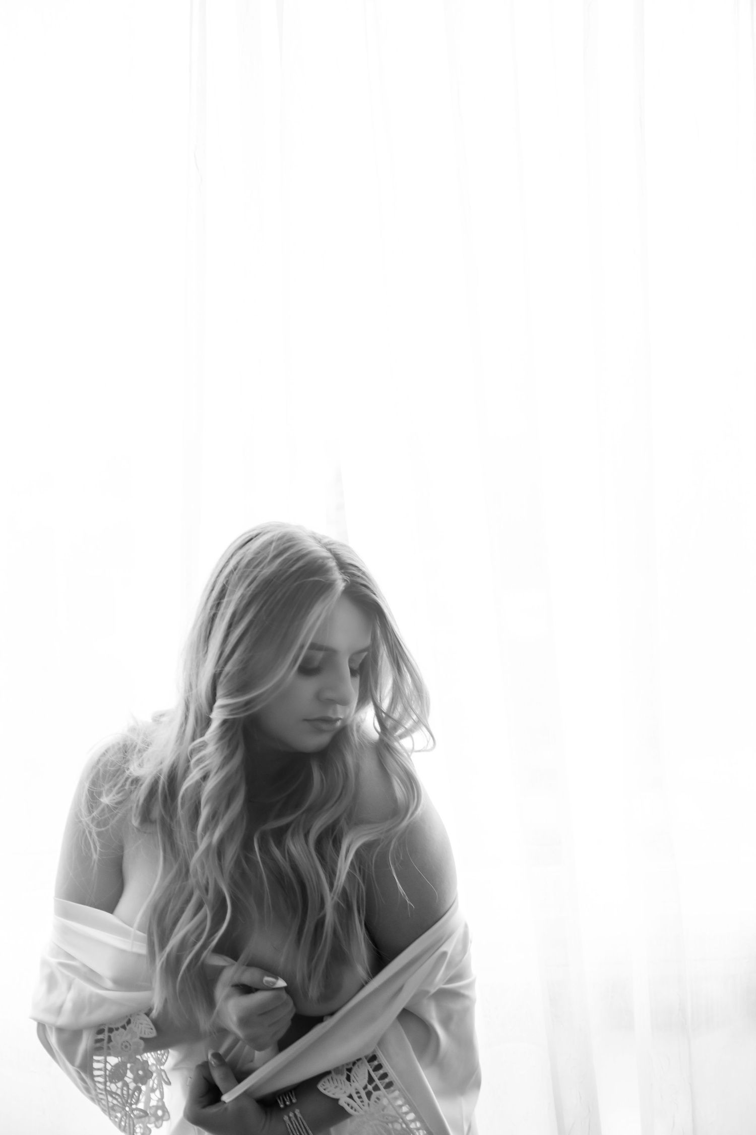 A dreamy boudoir photoshoot featuring someone in a white robe posing against a light background.
