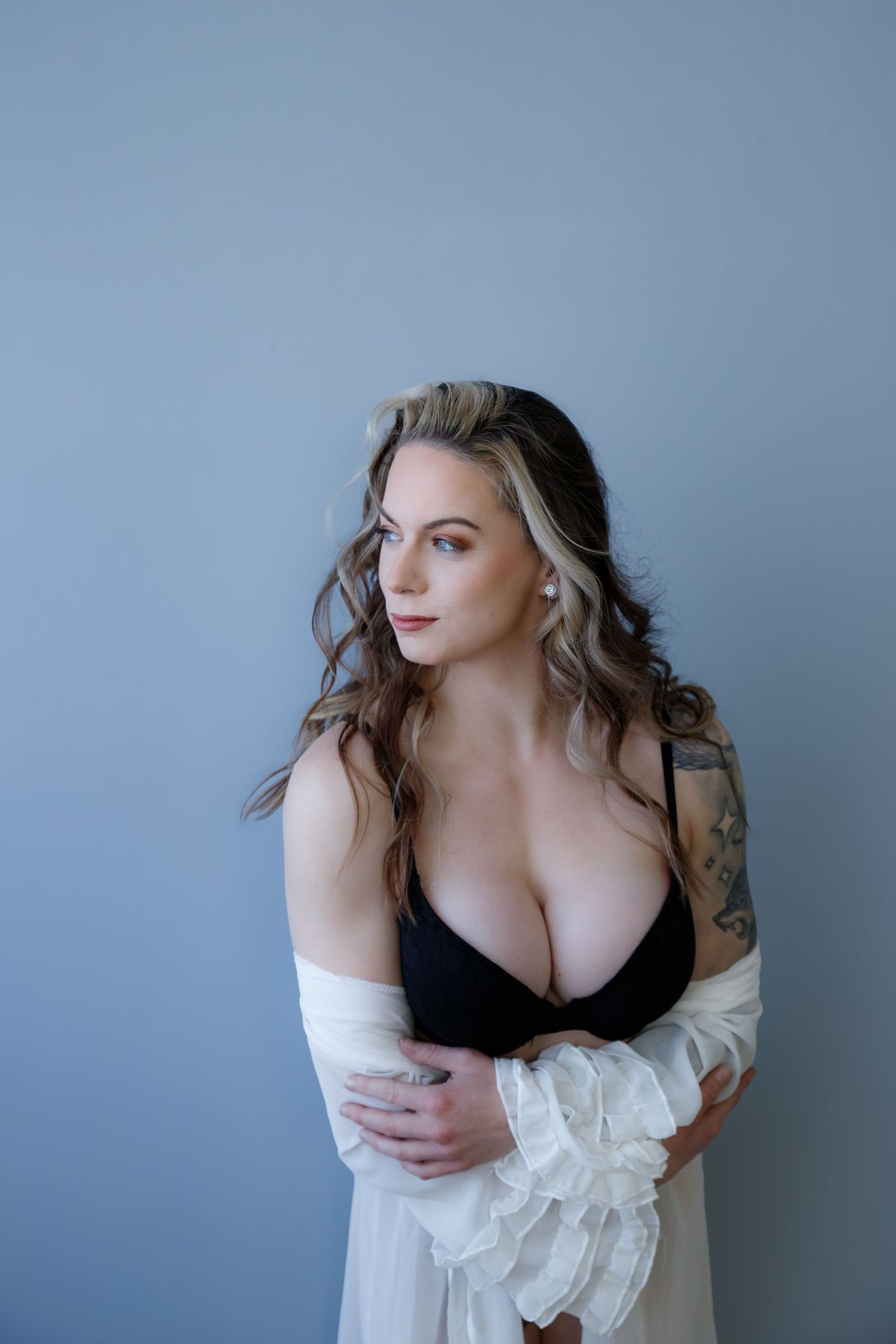Portrait of a model in black lingerie and white robe against grey background.