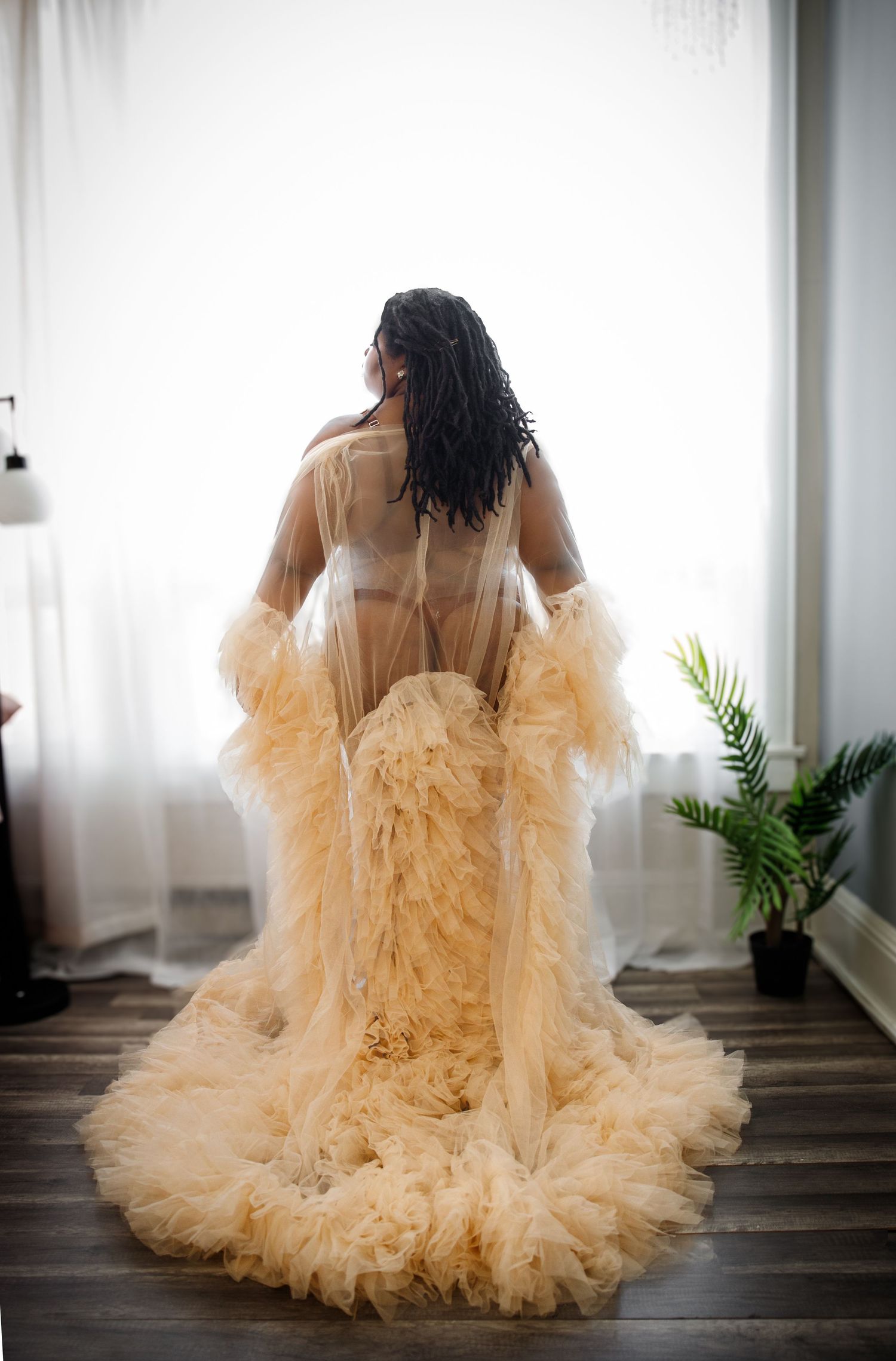 A bride in a flowing champagne-colored tulle gown sits gracefully on stairs in a series of artistic boudoir photos.