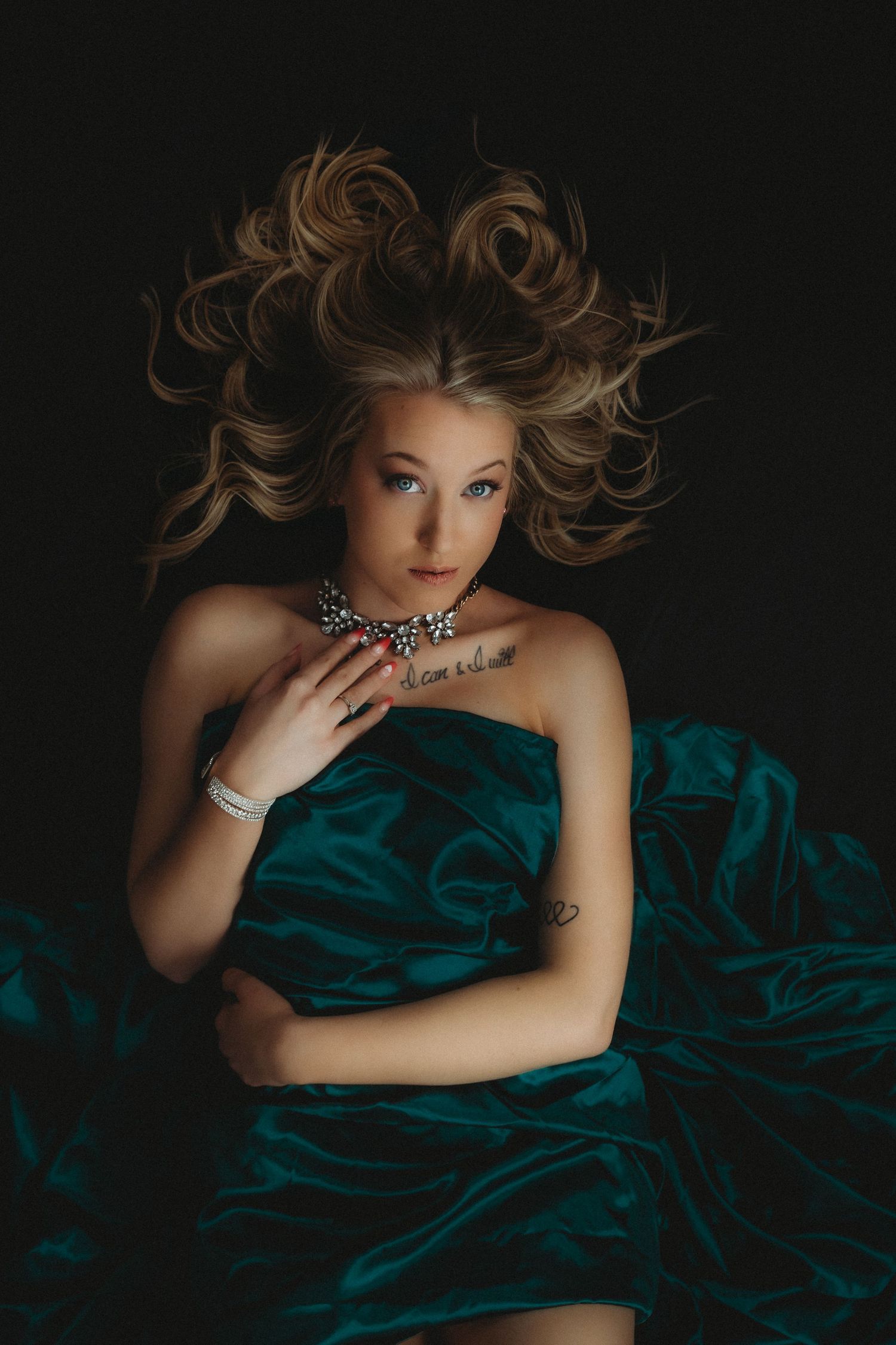 Dramatic fashion portrait with flowing brown hair against dark background wearing emerald green silk and sparkly necklace.