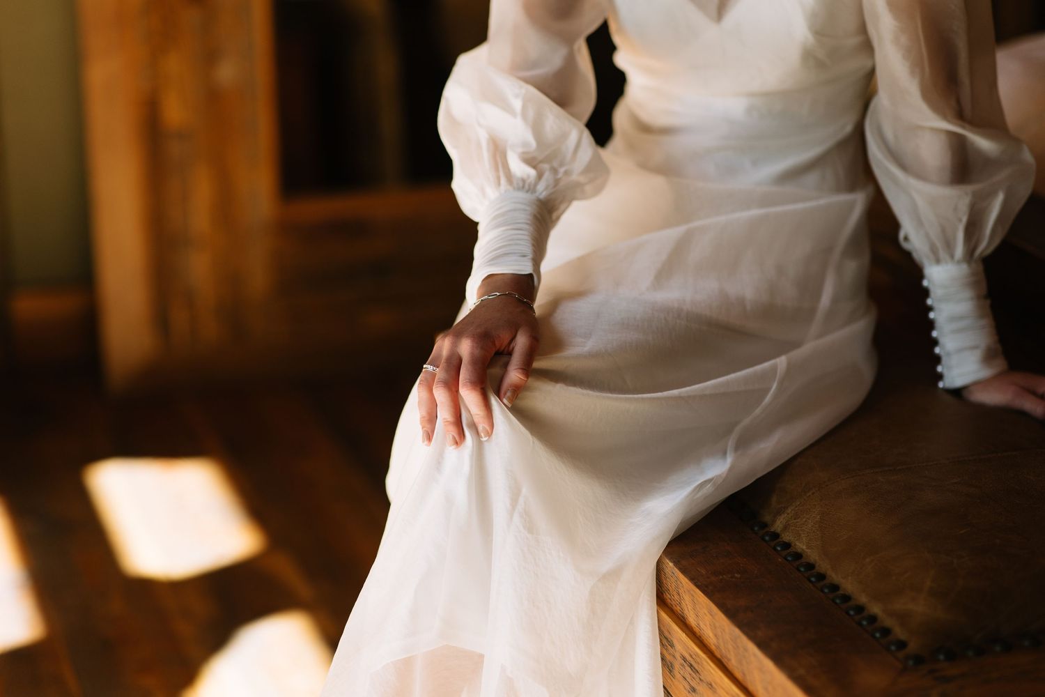 Elegant wedding dress skirt draped across wooden chair in warm natural lighting.