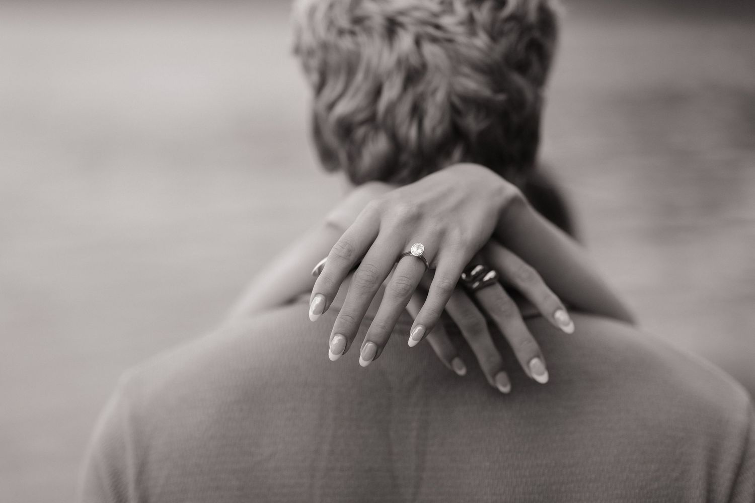 Graceful hands with jewelry rest gently on shoulders in an intimate black and white portrait.