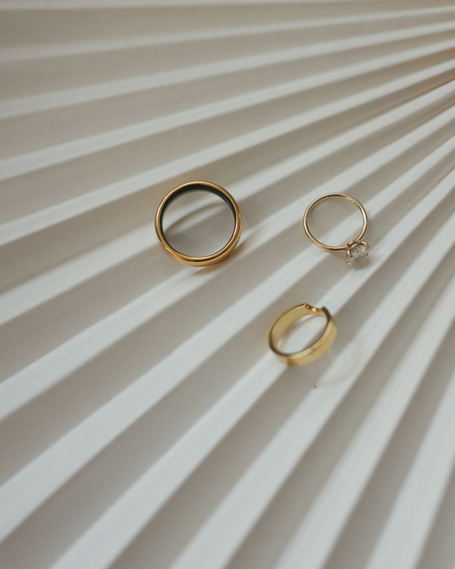 Three gold rings including a wedding band and engagement ring artfully arranged on a pleated white fabric backdrop.