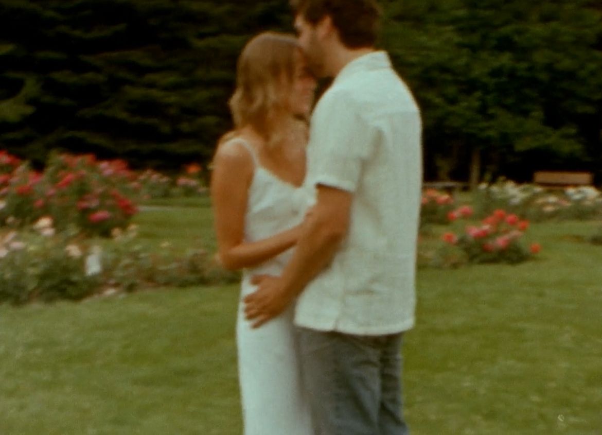 A romantic couple embraces in a garden with blooming roses, captured in a soft vintage film style.