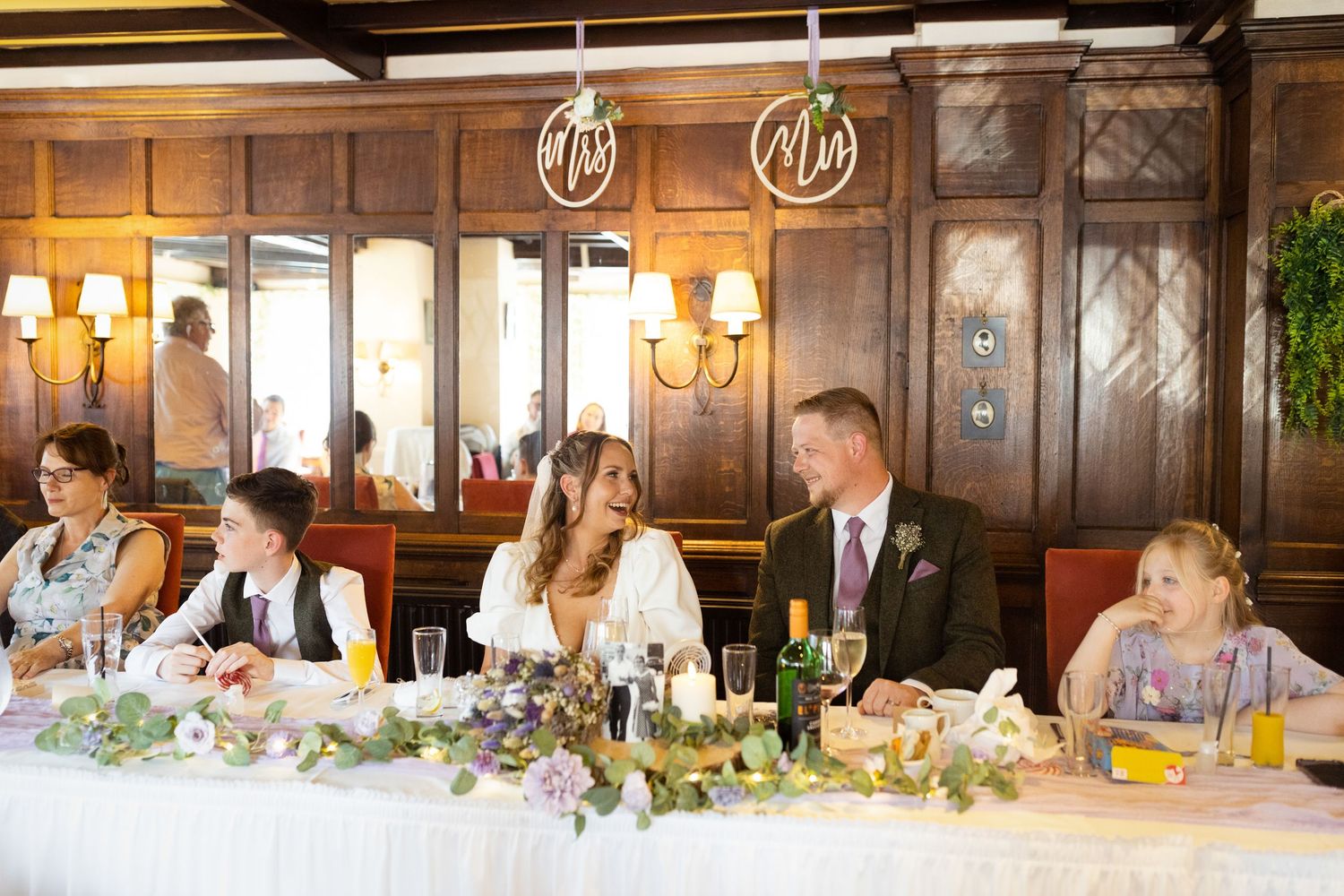 Elegant wedding reception dinner table with floral centerpieces and guests seated in a wood-paneled dining room.