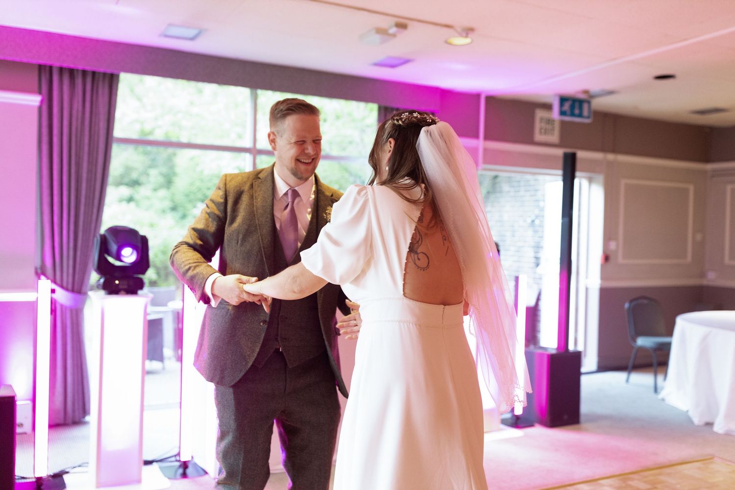 A newlywed couple shares a tender moment during their first dance at their wedding reception with pink lighting.