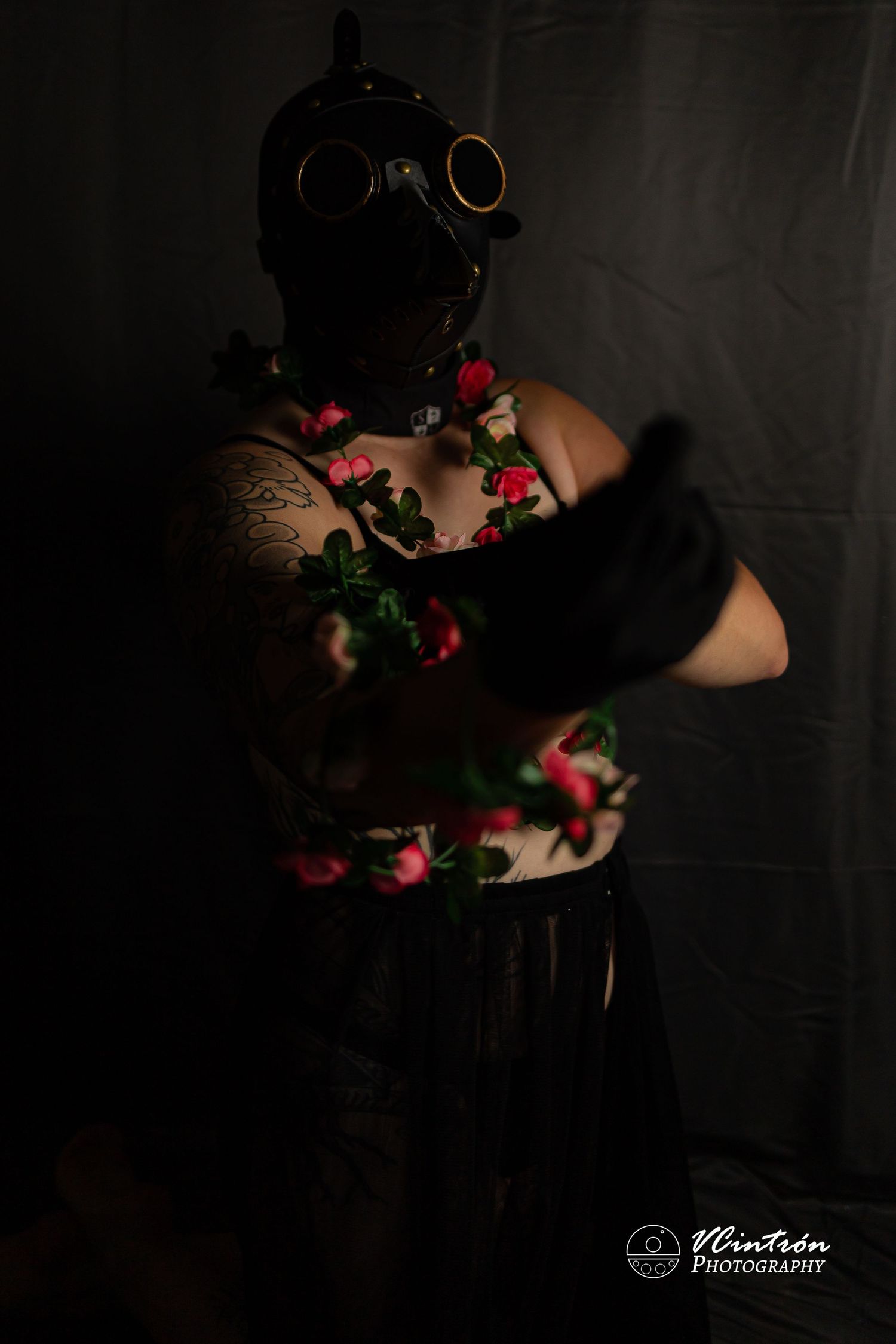 Dark moody portrait with gas mask and roses against black background with Phantasm Photography watermark.