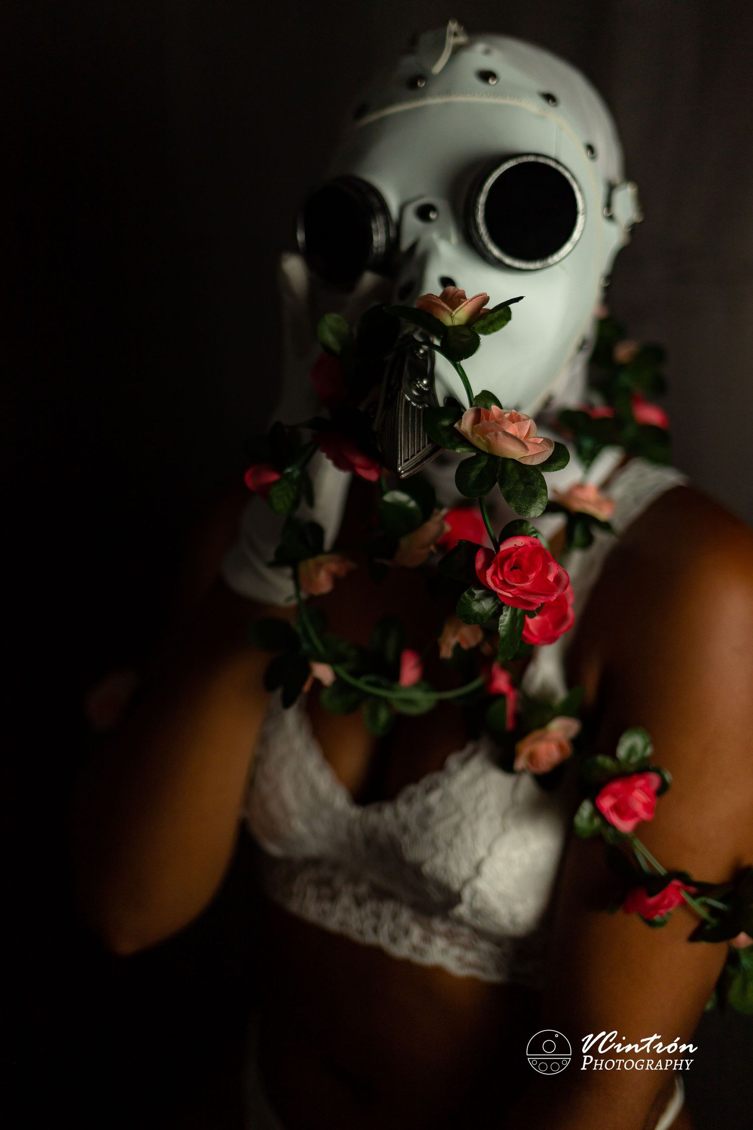 White porcelain mask with red roses and vines artistically draped around it in moody dark lighting.