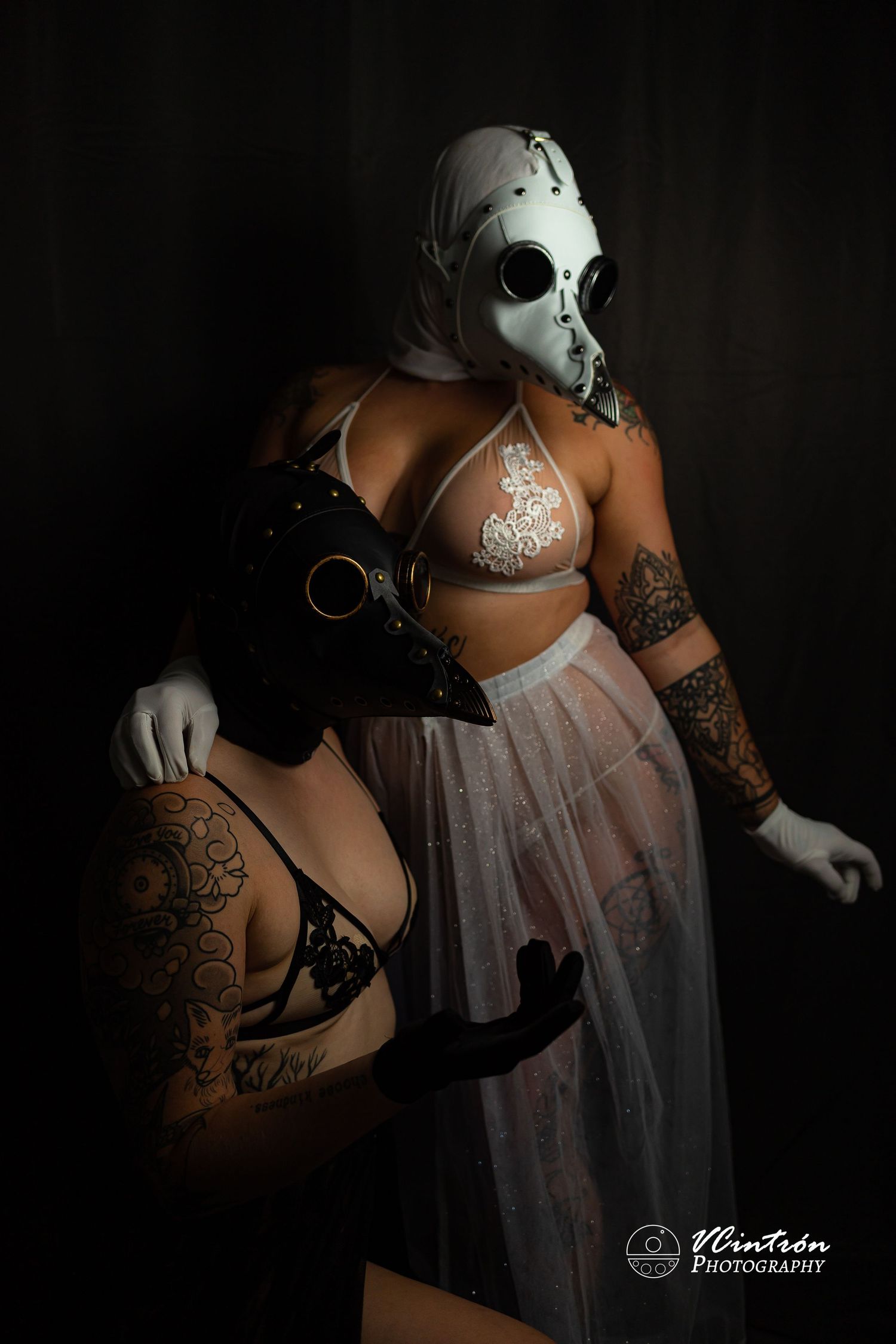Artistic dark boudoir photo featuring a person in white lace lingerie and mask with gothic tattoo aesthetic.