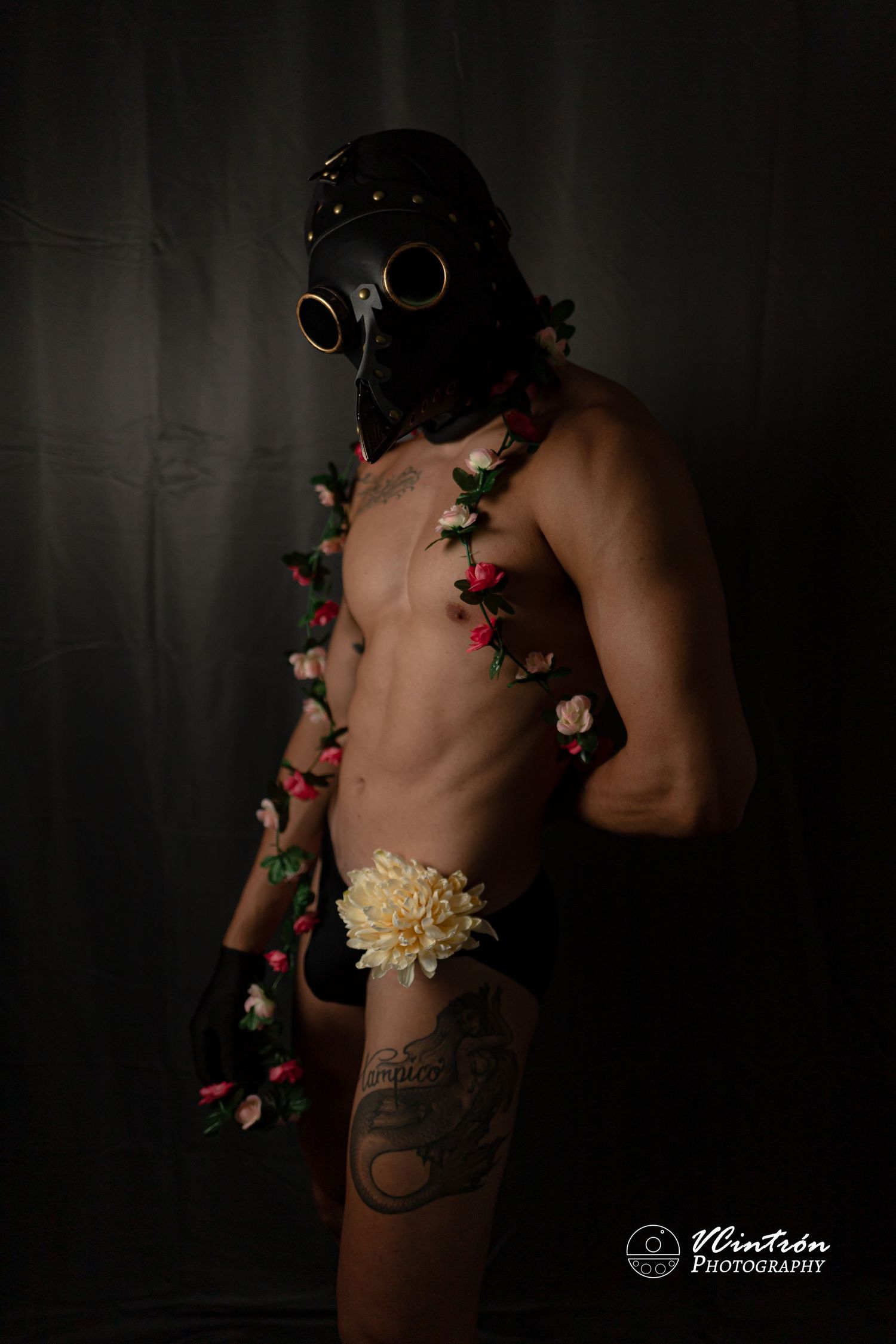 Artistic portrait featuring gas mask and floral elements against dark background with vintage photography styling.