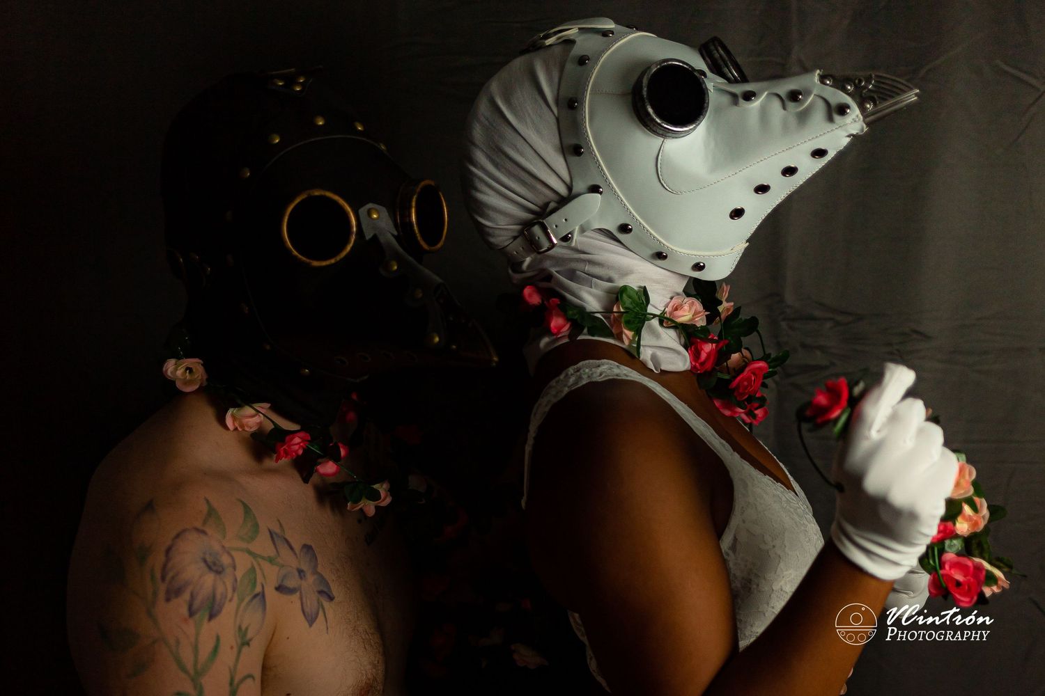 A stylistic portrait featuring a white plague doctor mask adorned with red rose petals against a dark background.