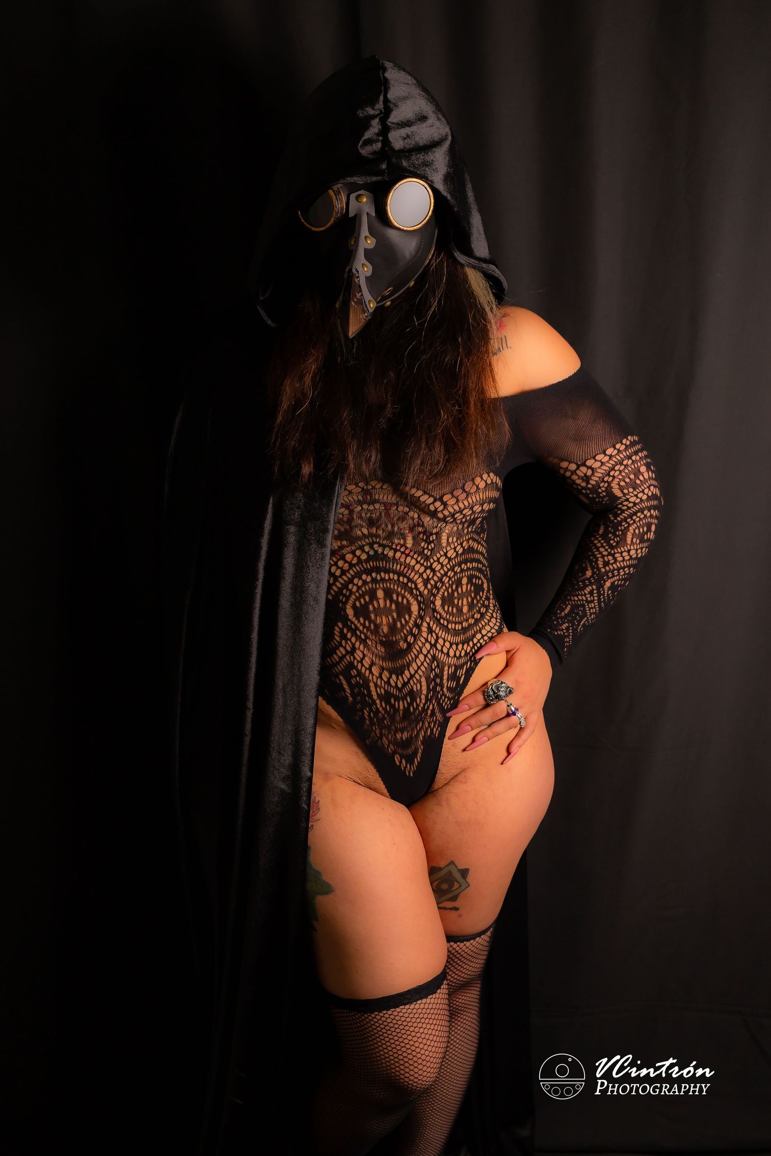 Artistic boudoir photo featuring a black lace bodysuit and cape against a dark dramatic background.