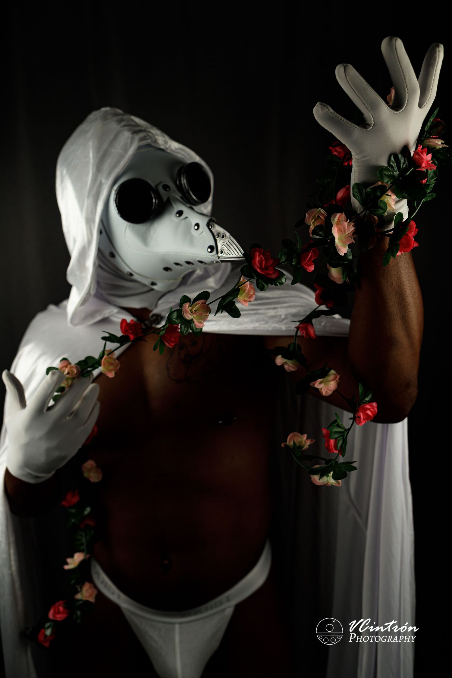 Artistic cosplay photo with white skull mask, gloves and dark background decorated with delicate red roses.