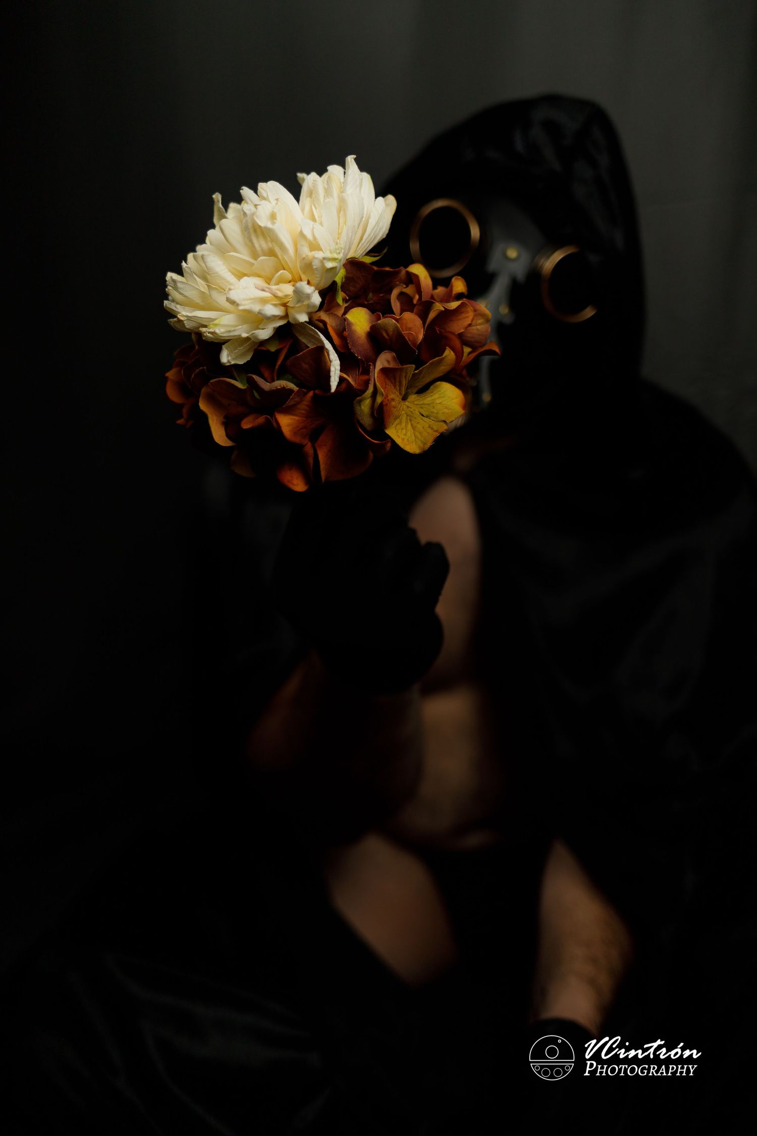 Dark moody photograph of a bouquet with white chrysanthemum and brown flowers held against shadowy background.