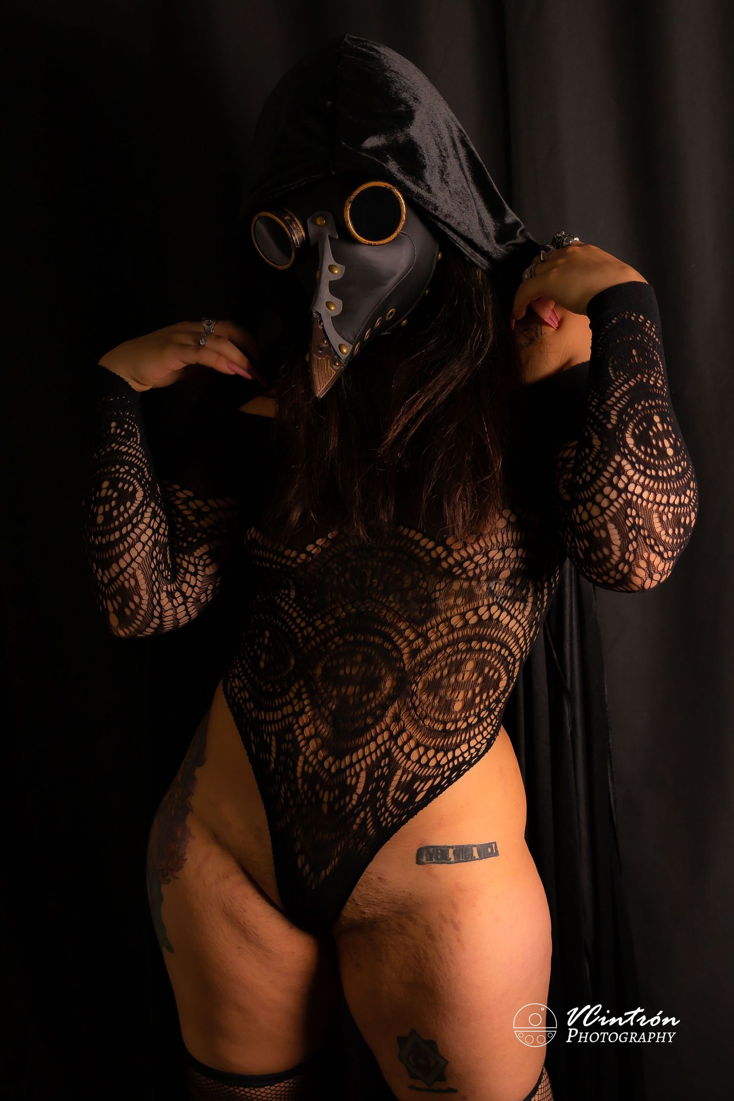 Dark artistic portrait featuring a plague doctor mask, black lace bodysuit and moody lighting creating a gothic atmosphere.