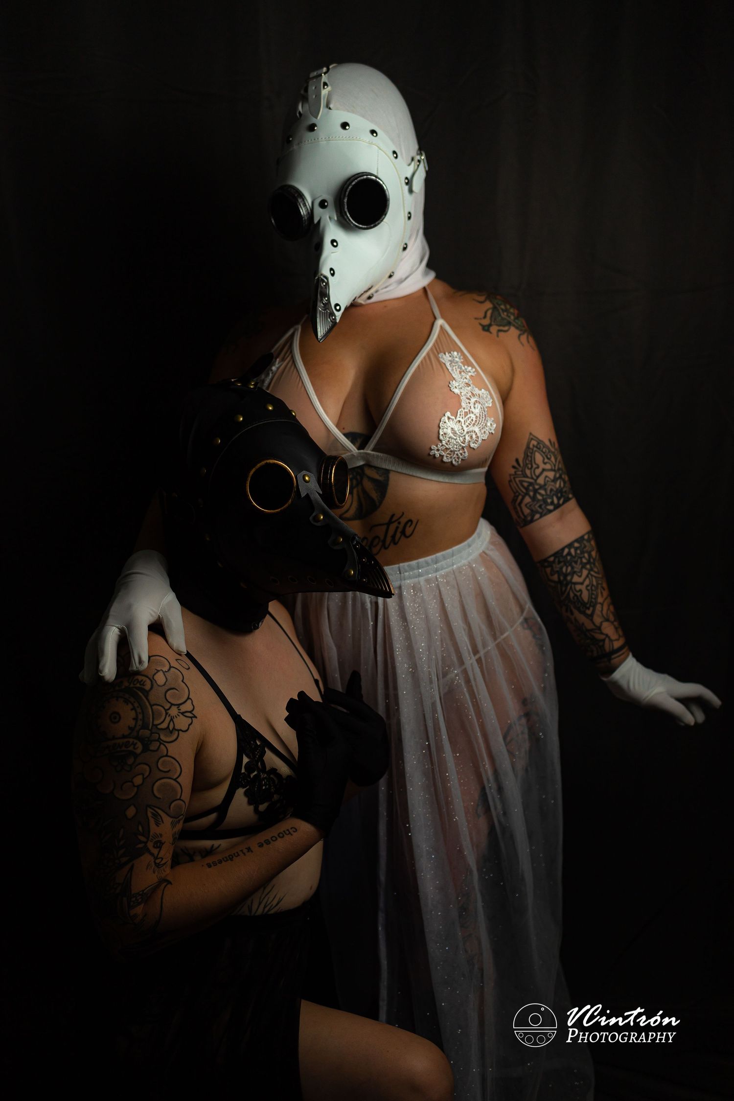 Moody artistic portrait of someone in a white horror mask, lingerie and sheer skirt against dark background.