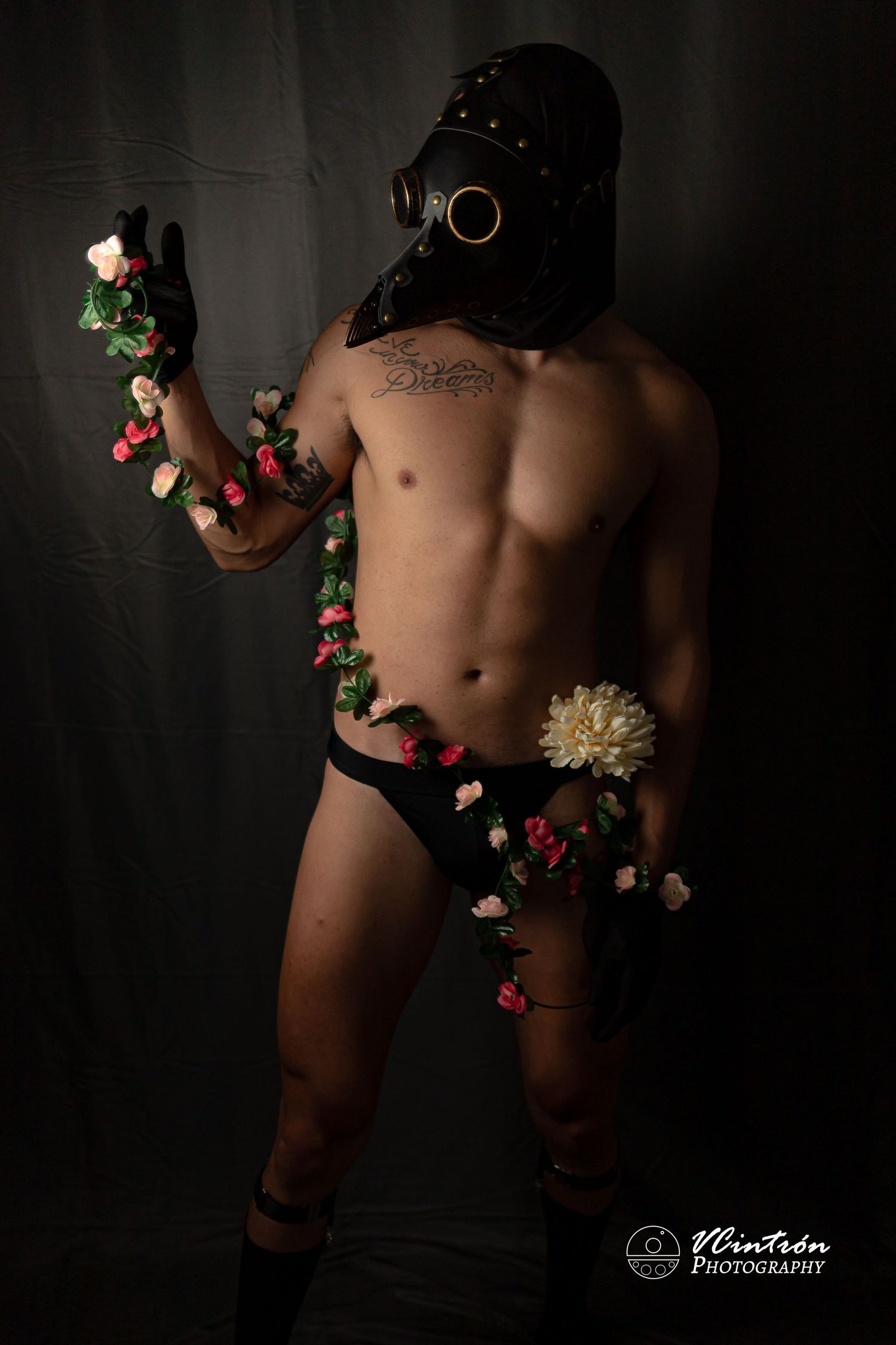 Artistic dark portrait of person in gas mask and minimal clothing posing with roses wrapped around their body.