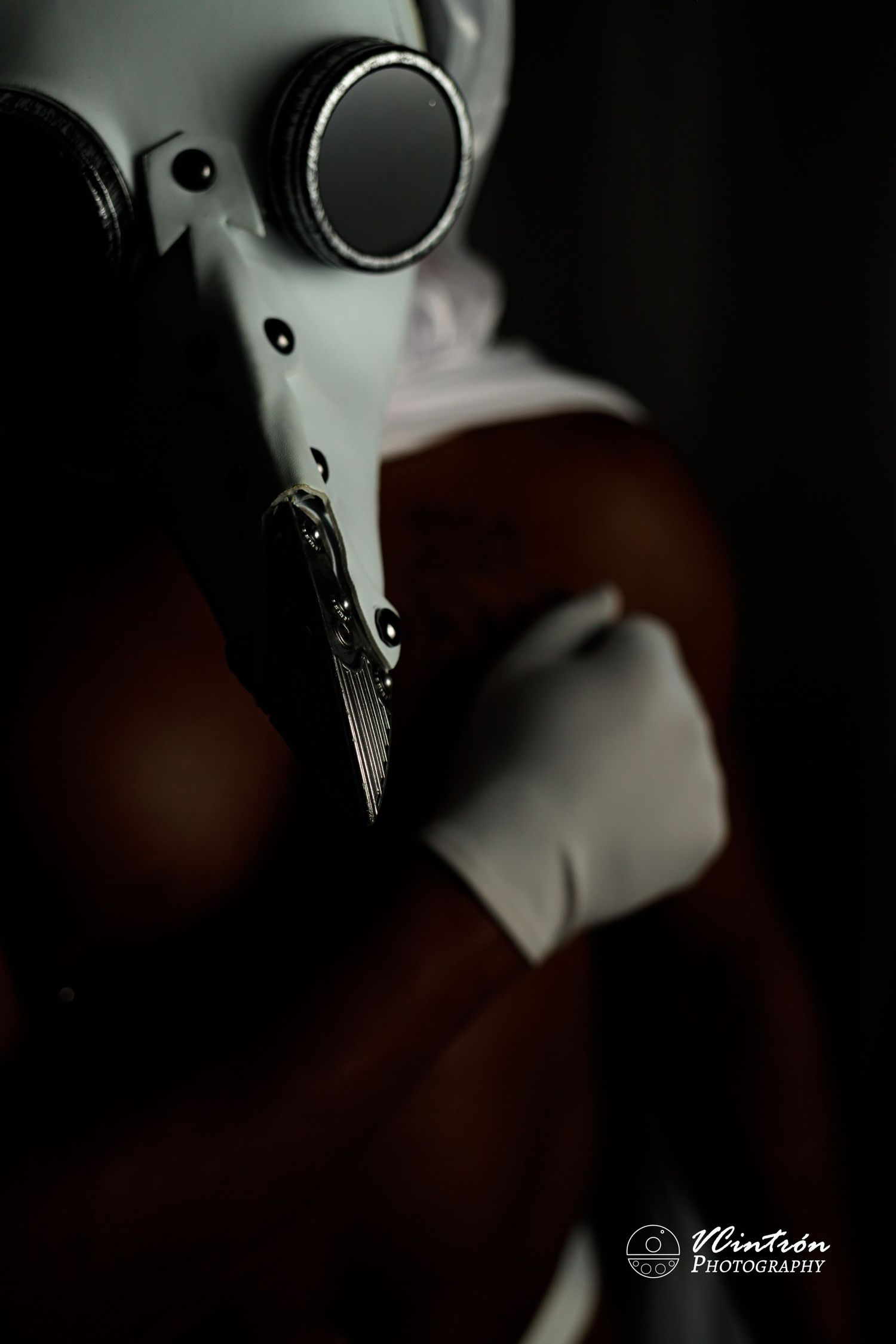 A close-up black and white artistic photograph shows a plague doctor mask against a dark background.