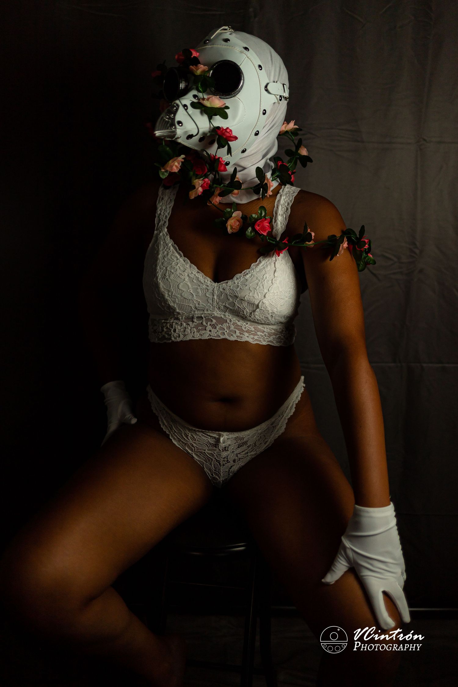 Moody boudoir photo with white lace lingerie and Halloween mask against dark background with red butterfly accents.