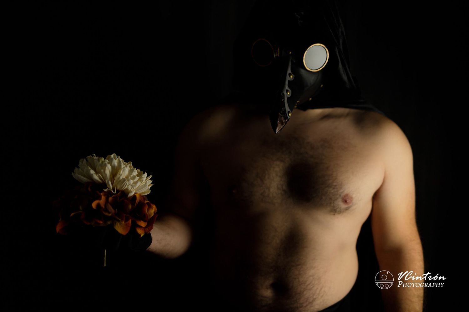 Artistic dark portrait of a shirtless person holding a bouquet of flowers against a black background.