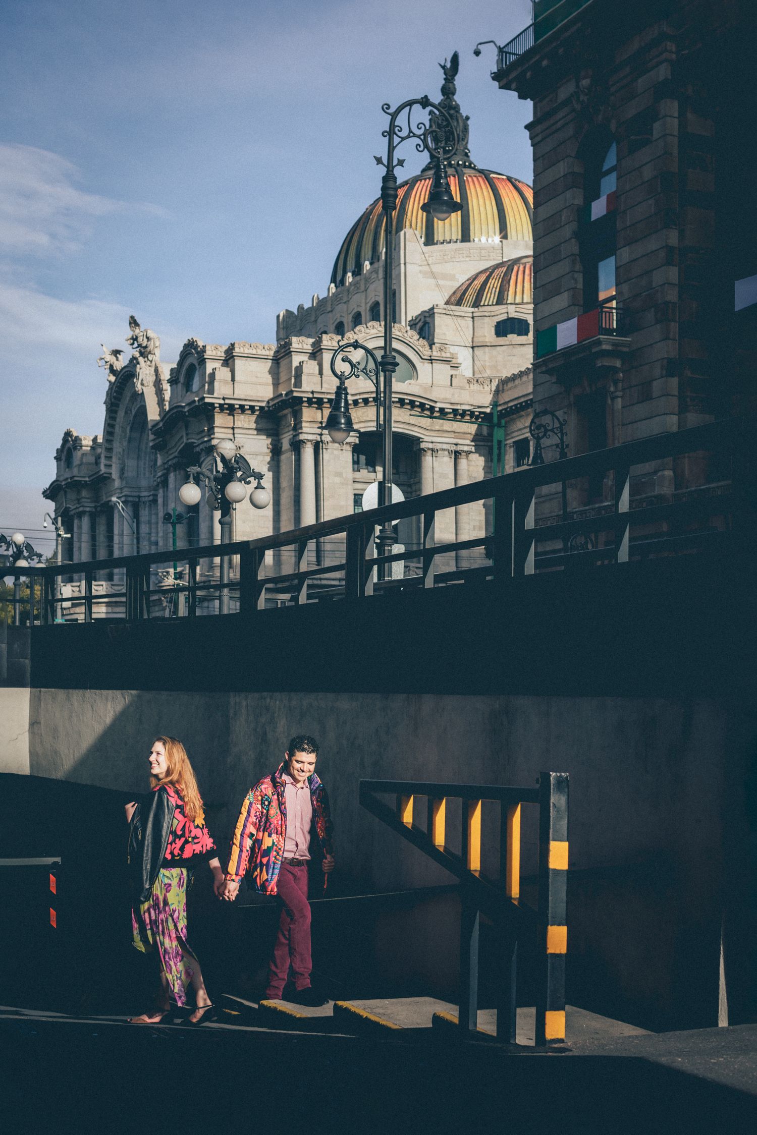 Two people stand in shadow beneath ornate European architecture with a golden domed building visible above.