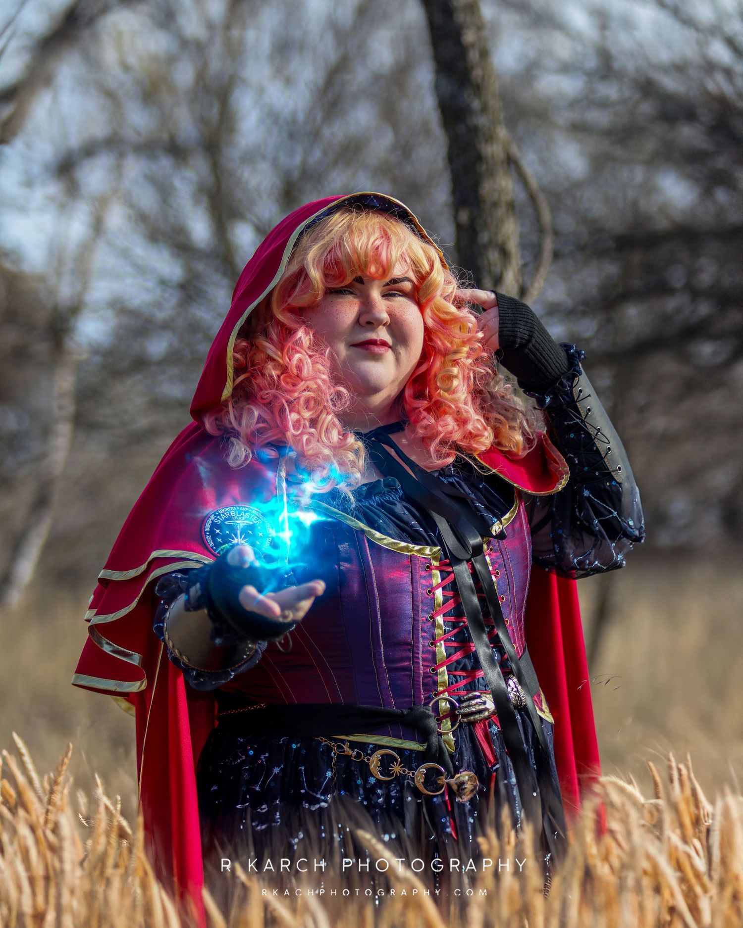 Fantasy cosplayer in medieval dress holds glowing blue magical effect in outdoor setting.