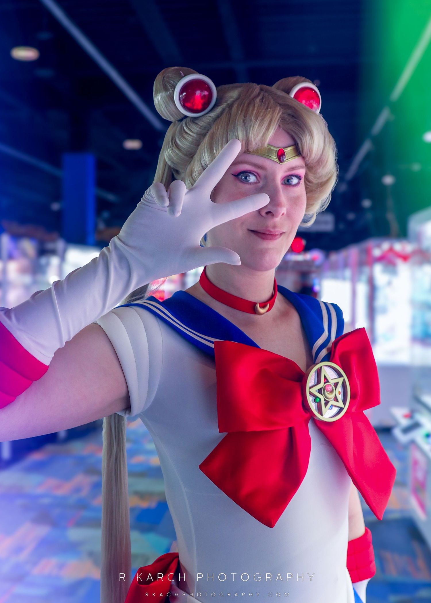 Sailor Moon cosplayer making peace sign gesture with white gloved hand against blue lights.